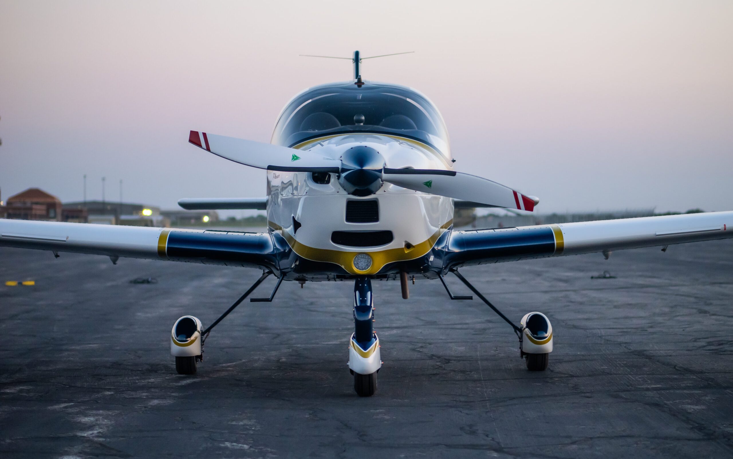Sleek propeller aircraft with a large canopy and tricycle landing gear, photographed at a low angle on the airfield during twilight